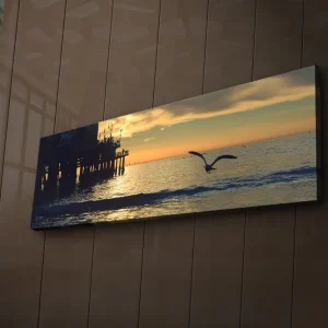 Extra rabatt Canvastavla med LED-belysning 30x90 cm - Solnedgång över havet med en fågel i flykt Orange / Blå / Grå - Inredning